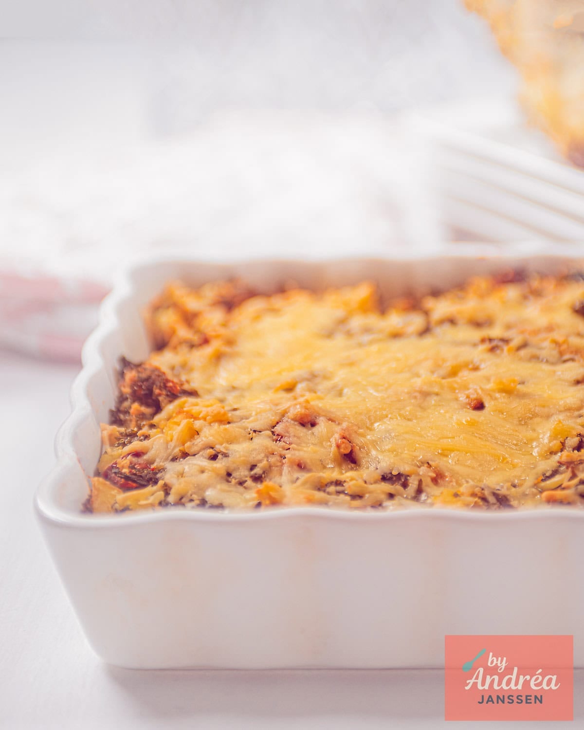 A portion of a white oven dish with a mashed kale with tomato and cheese, gratinated.