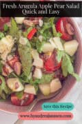 A portion of a pink bowl with a salad of arugula, tomato, pear, apple, and pistachios. A caption reads: Fresh Arugula Apple Pear Salad – Quick and Easy