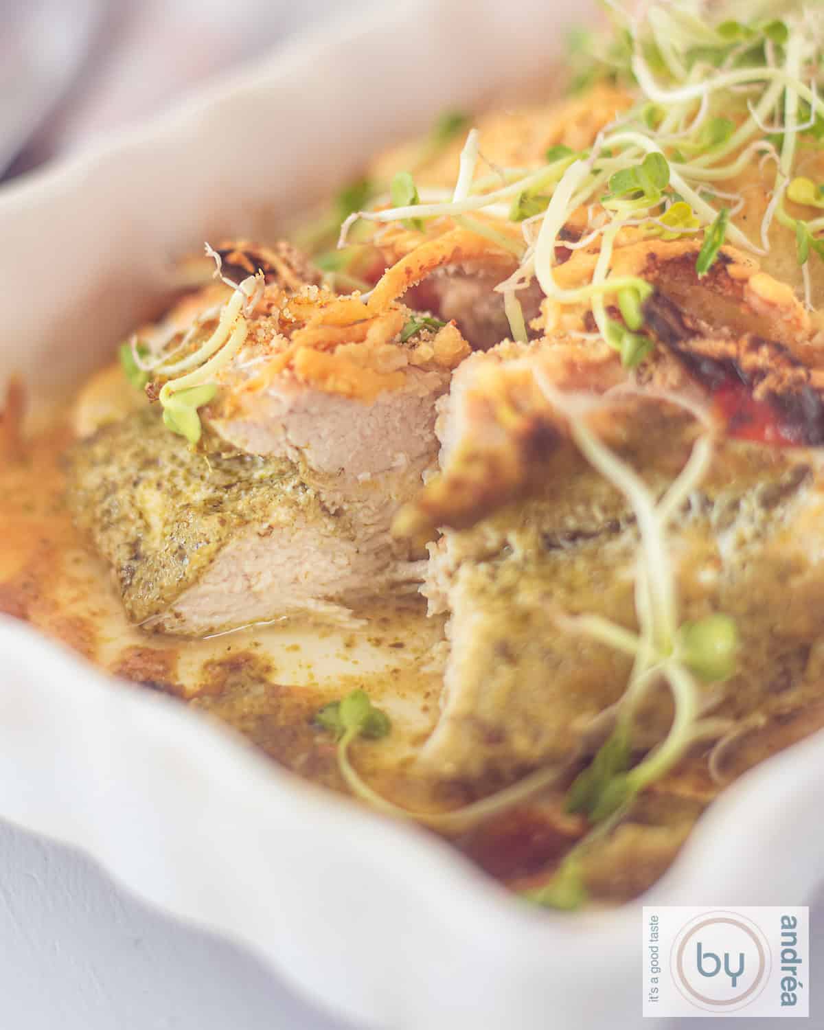 A white oven dish with chicken fillet, cut open with pesto and cheese.