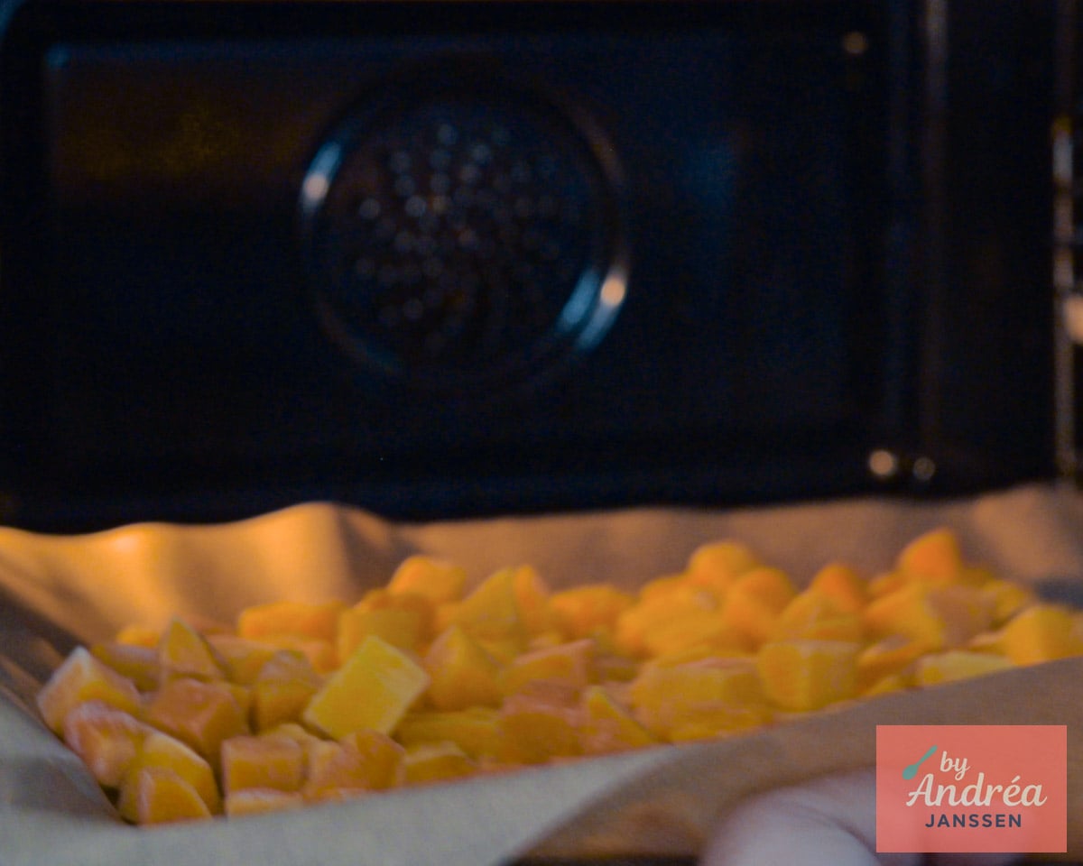 Pompoenblokjes op een met bakpapier beklede bakplaat in de oven.