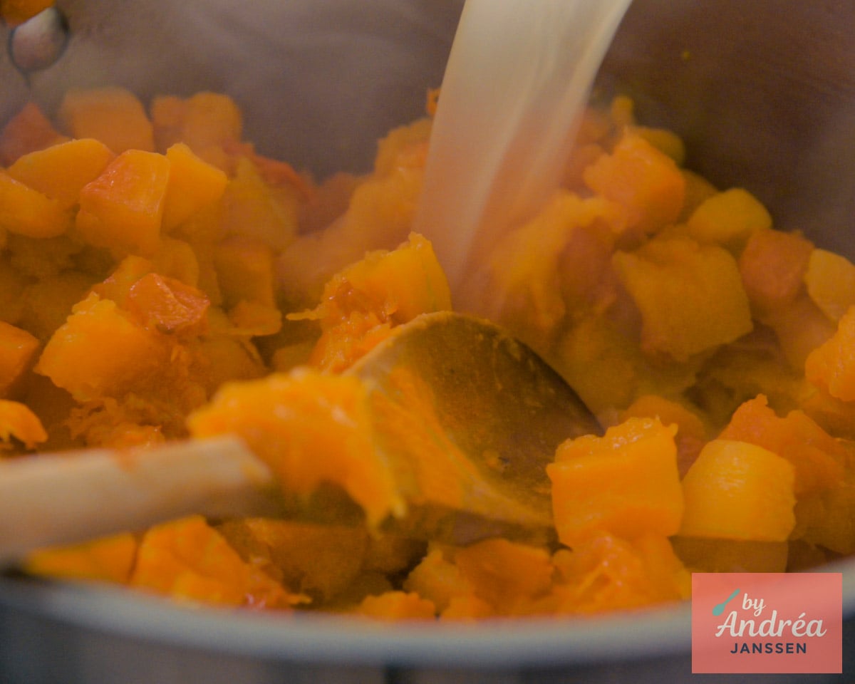 Bouillon stroomt in een pan met geroosterde pompoenblokjes en specerijen.