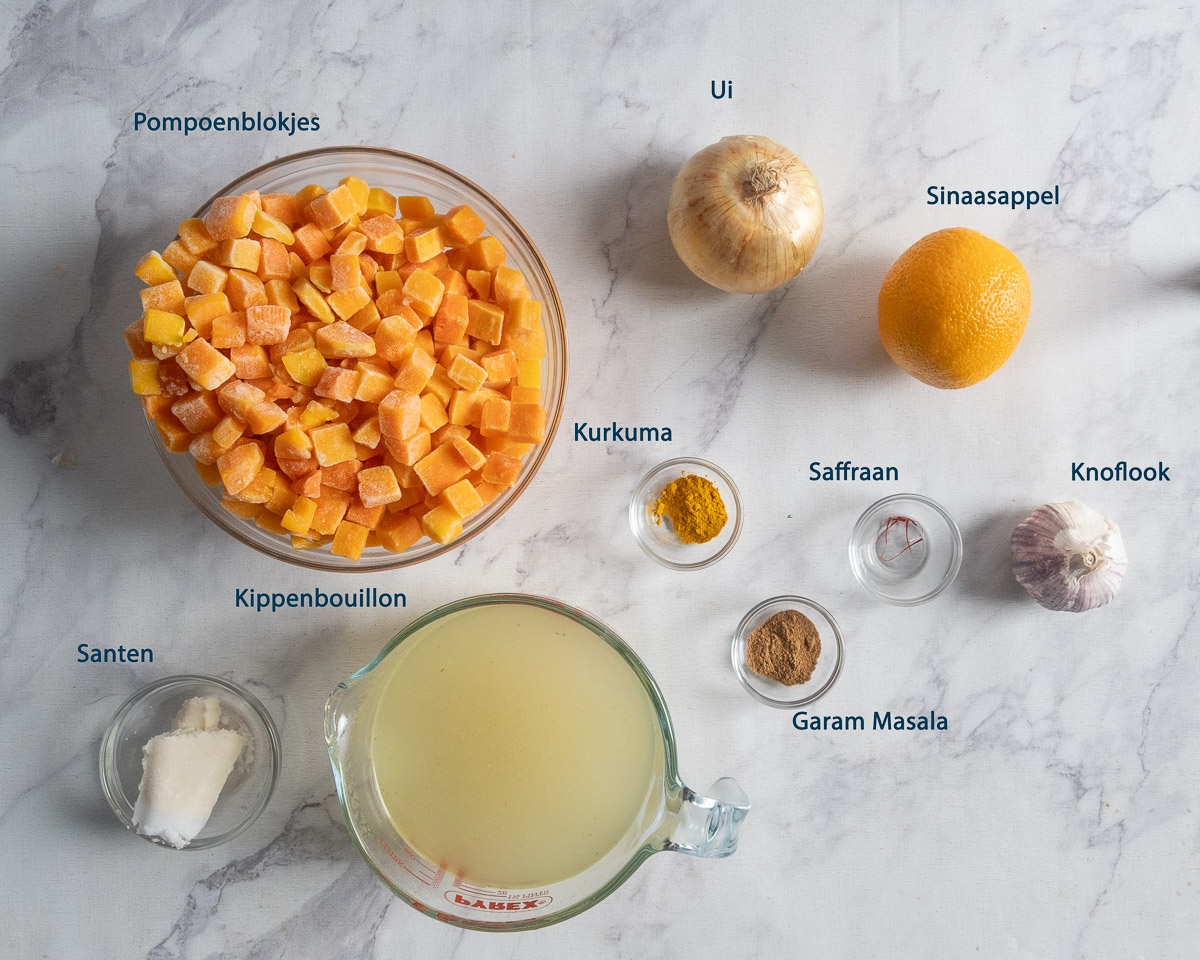 ngrediënten met Nederlandse labels: pompoenblokjes, ui, sinaasappel, knoflook, saffraan, kurkuma, garam masala, kippenbouillon en santen.