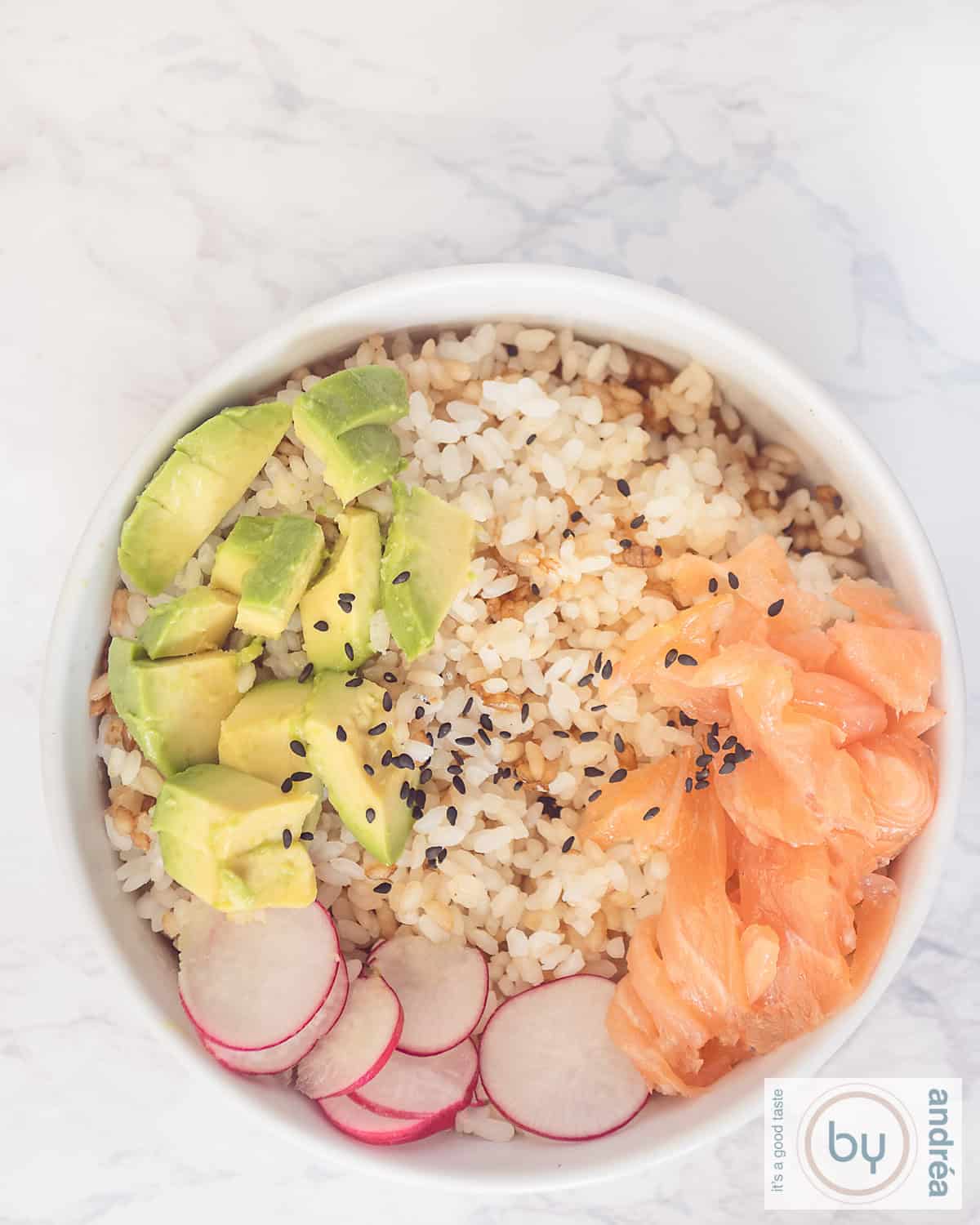 Een foto van bovenaf van een witte kom op een marmeren ondergrond. Gevuld met sushi rijst, radijs, avocado, zalm en sesam.