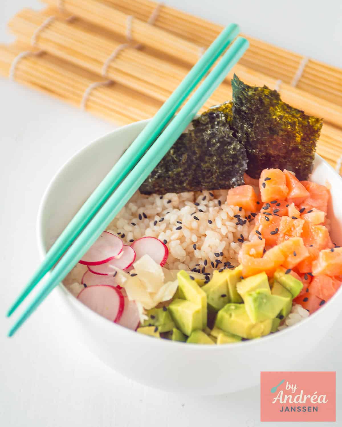 A picture with a white bowl filled with smoked salmon, avocado cubes, radishes, nori sheets and sushi rice