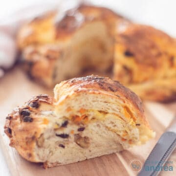 A square photo of a sweet bread wreath with a piece cut out. It is in the foreground.