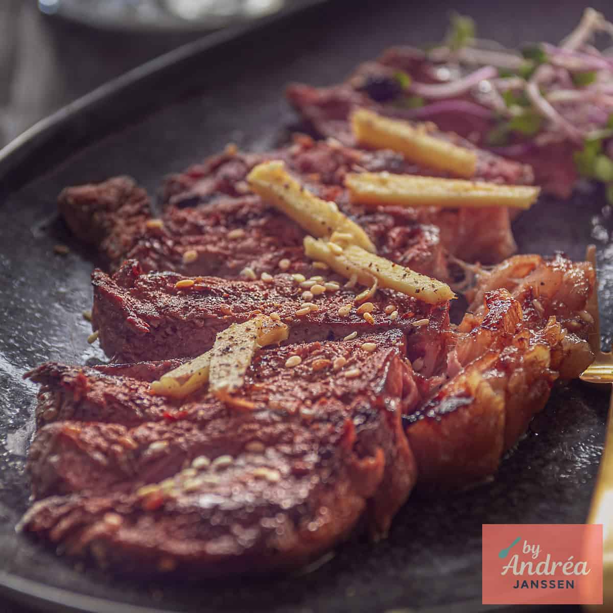 A square photo with a black bowl with strips of sirloin steak and soy sauce ginger sauce