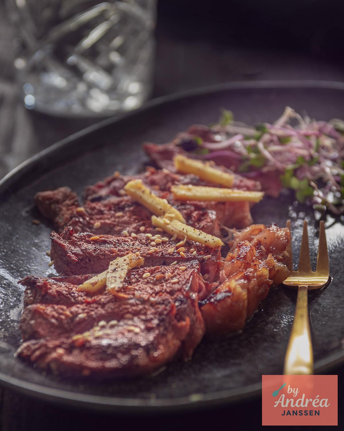 A black bowl with strips of entrecote with soy sauce and ginger sauce and a golden fork.