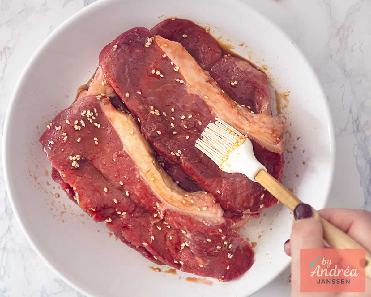 A white dish with sirloin steaks covered with the marinade