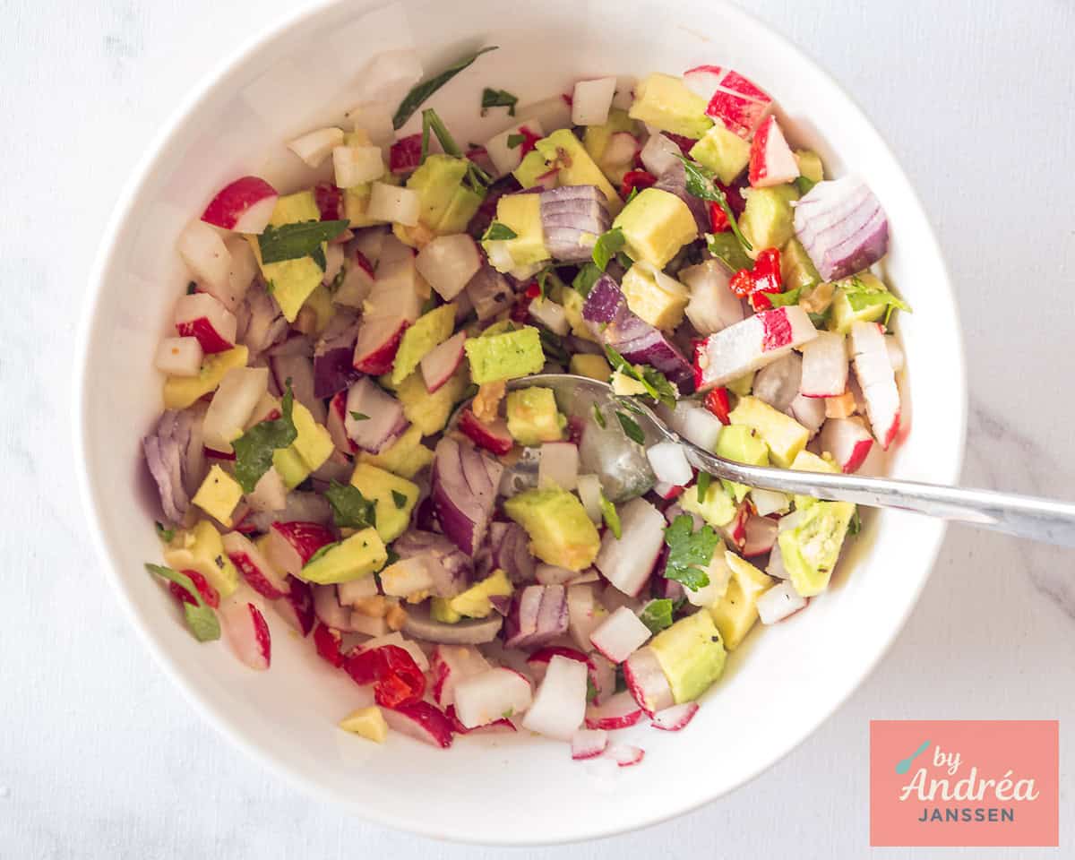 Preparing avocado radish salsa in a white bowl