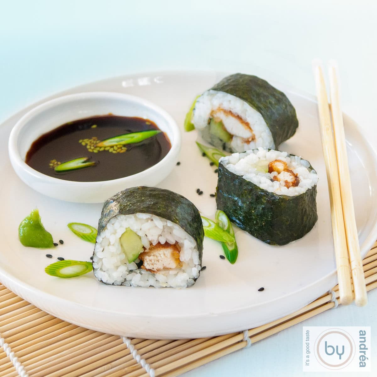 A square photo of 3 rolls of sushi with chicken and cucumber and soy sauce on a white plate.