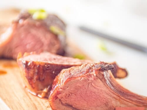 Three pieces of rack of lamb with an Asian marinade on a wooden board.