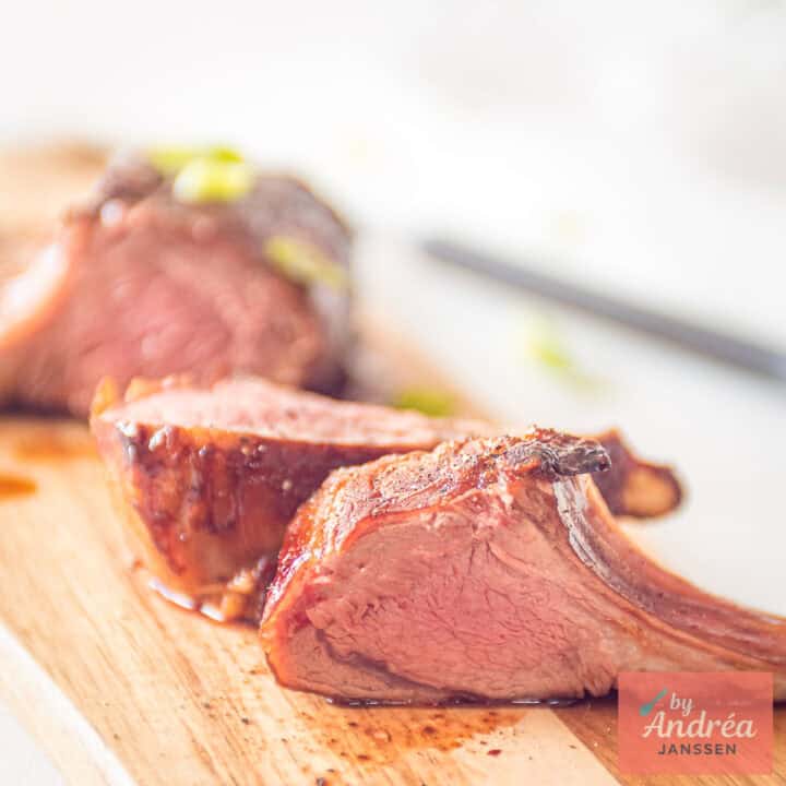 Three pieces of rack of lamb with an Asian marinade on a wooden board.
