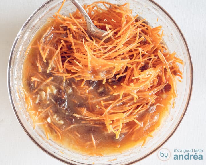 The wet ingredients of the carrot cake are mixed with carrot, walnuts and raisins in a glass bowl.
