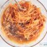 The wet ingredients of the carrot cake are mixed with carrot, walnuts and raisins in a glass bowl.