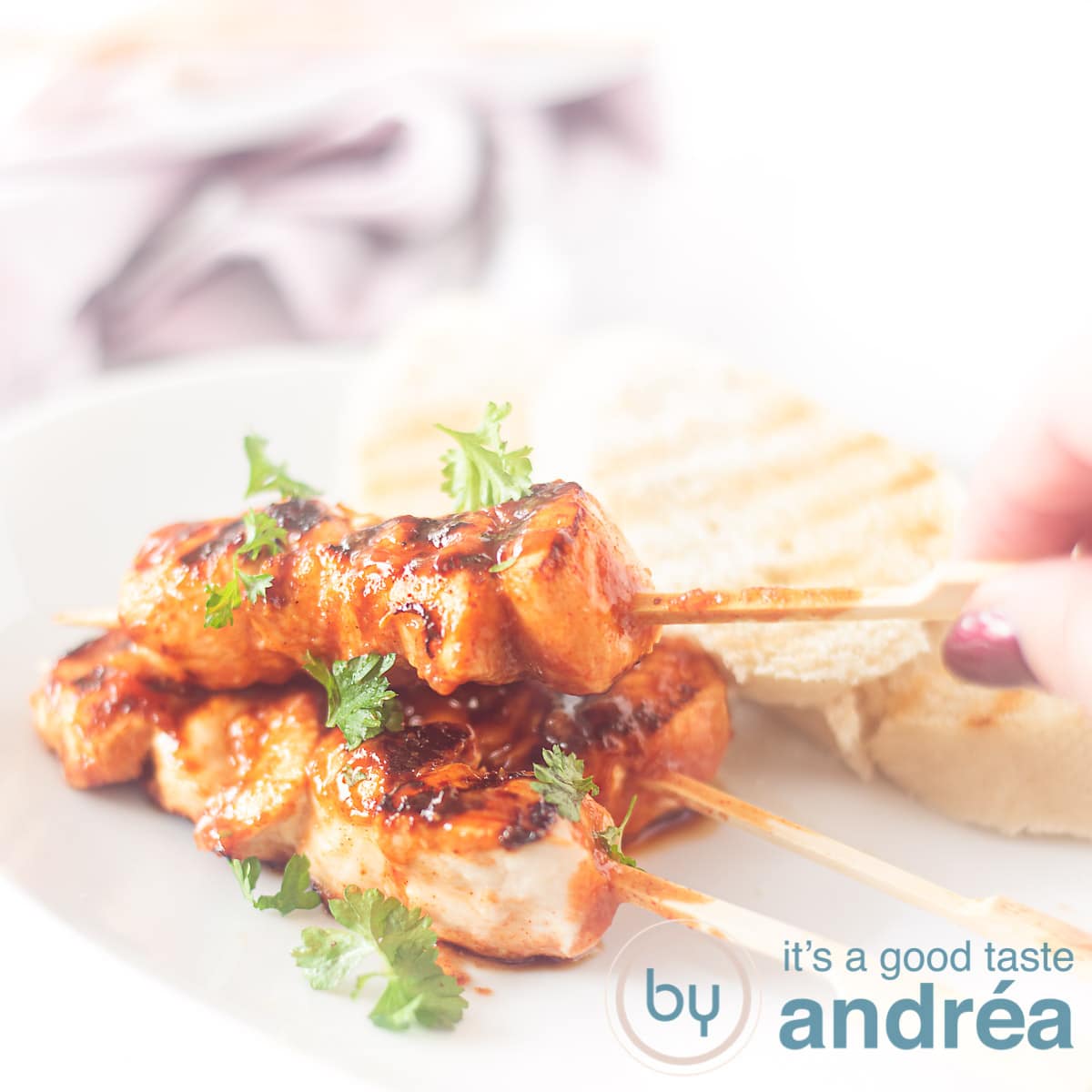 A square photo with a white plate with three chicken skewers, a hand grabbing one and three slices of toast