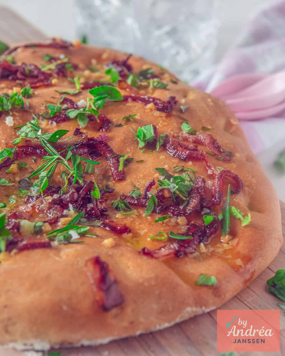 Focaccia met kruiden, rode ui, knoflook en boter op een houten plank.