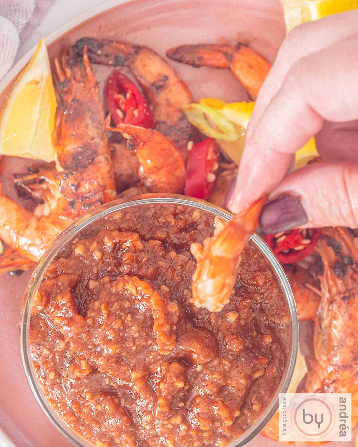 A top-down photo of grilled shrimp with lemon, pepper dipped in satay sauce.