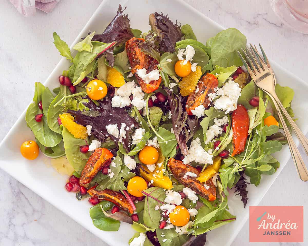 A wide shot of a salad with pomegranate, sun-dried tomatoes, feta and golden apple