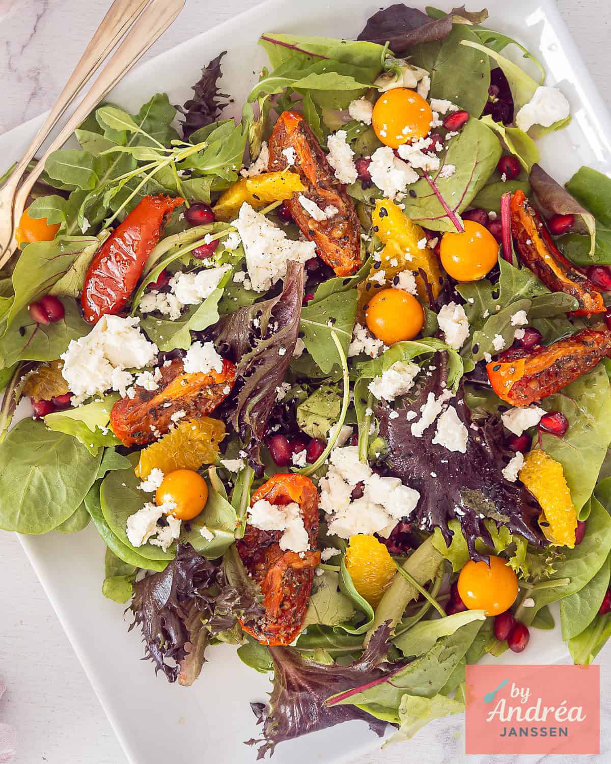 A top-down photo of a mixed salad with orange, feta, golden berries, sun-dried tomatoes