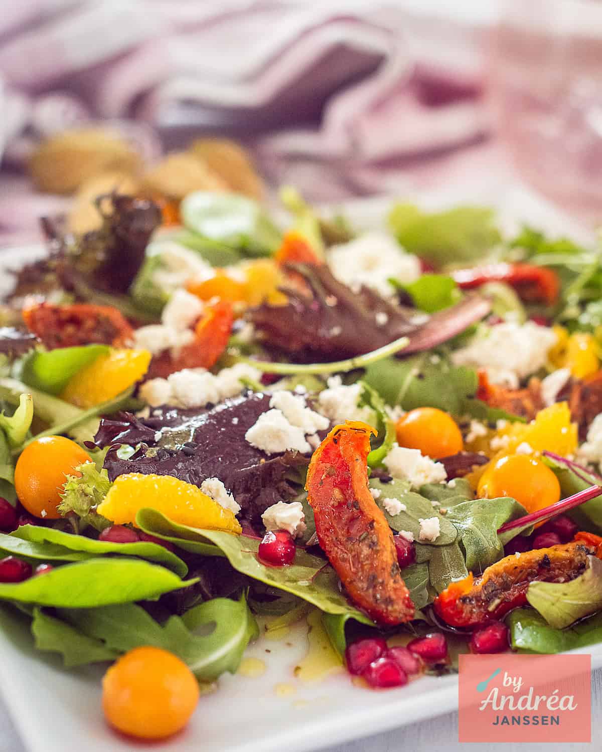 A salad with pomegranate, golden berries, sun-dried tomatoes and feta on a white plate.