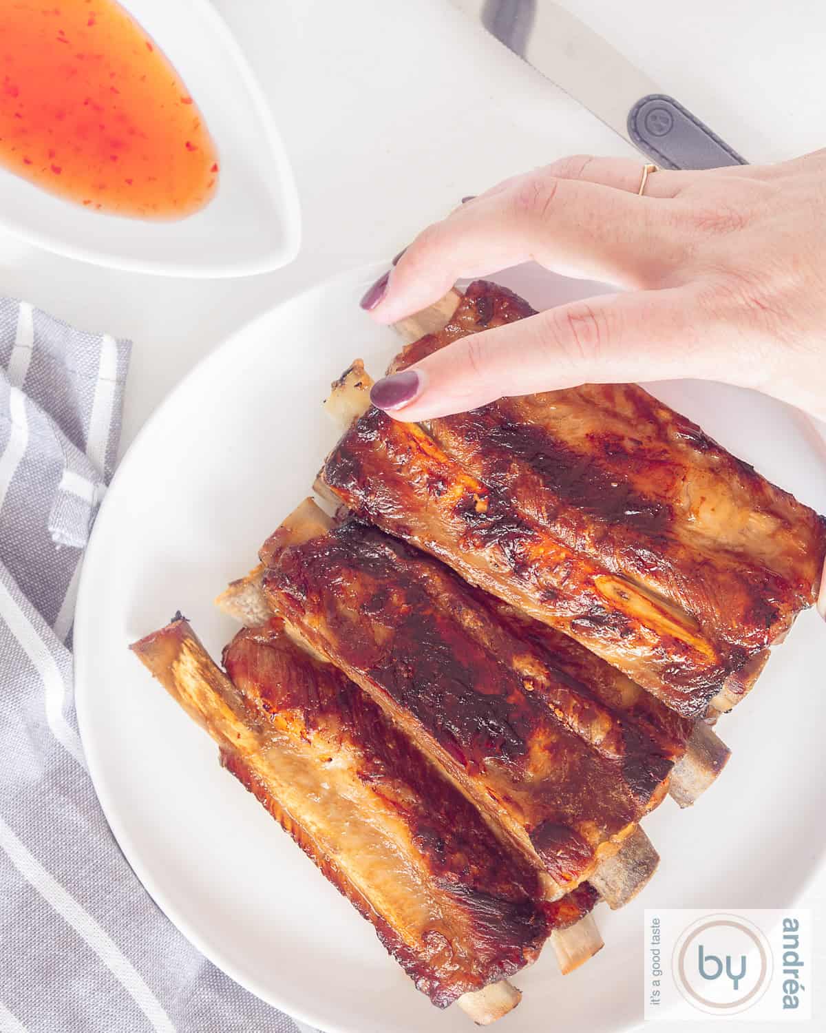 An overhead shot of a plate of ribs. A hand grasps a sticky rib.