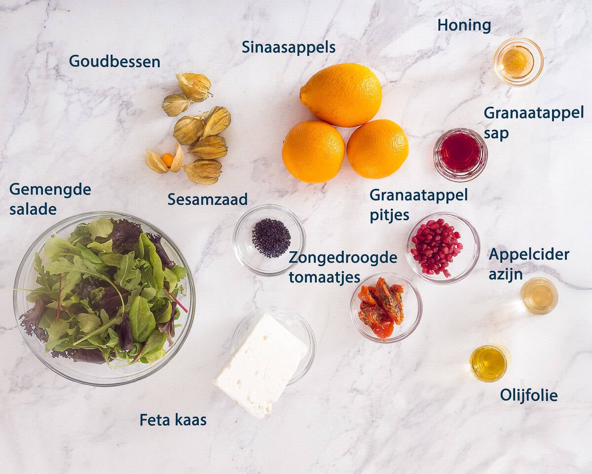 Ingredienten Sinaasappel Salade Met Granaatappel En Feta op een wit marmeren ondergrond en een tekstbeschrijving