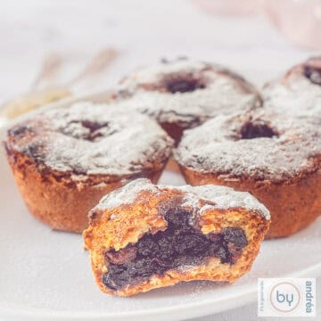 A square picture with fruit mince pies on a white plate. One is in half and you can see the fruit mince filling.