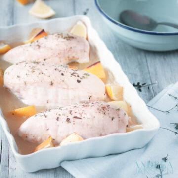 a white casserole with chicken, lemon and thyme. A blue bowl and white cloth