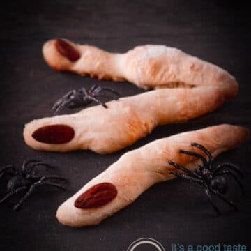3 creepy bread fingers with spiders on a wooden board