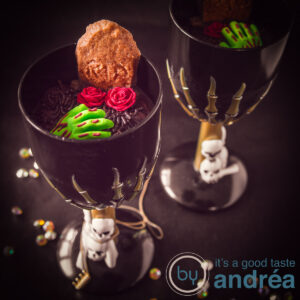 a square photo with two black glasses with skulls filled with chocolate dirt, zombiehands, roses and RIP graveyard cookies