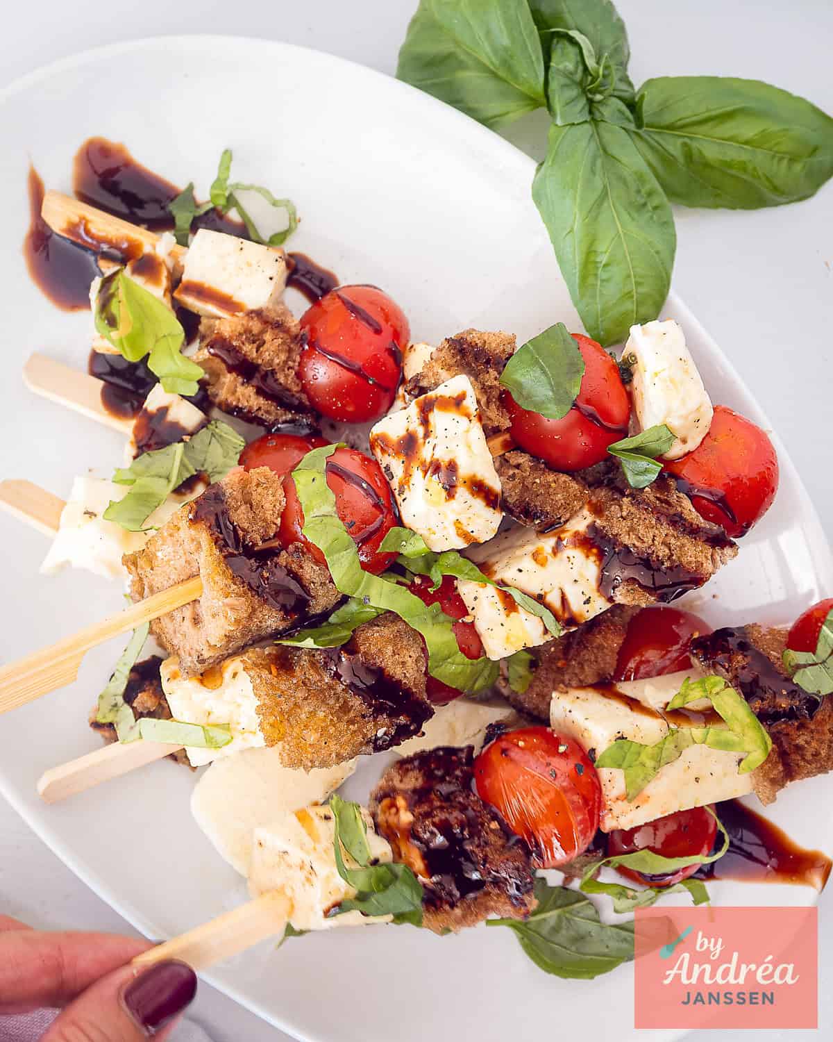 A top-down photo of a plate of halloumi skewers with tomato, bread with garlic oil, basil and balsamic cream