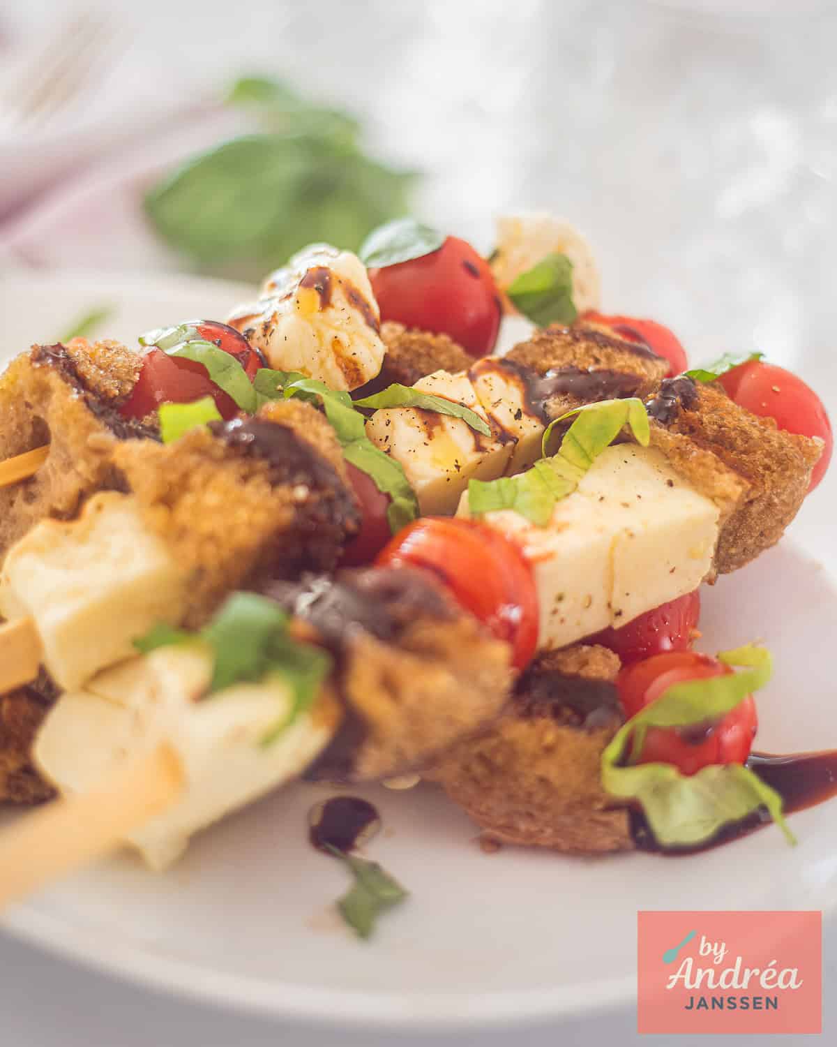 A white plate with caprese halloumi kebabs with balsamic cream