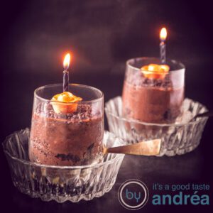 a square photo with two glass bowls and in there two glasses filled with chocolate mousse, a golden rose and a black candle lit.