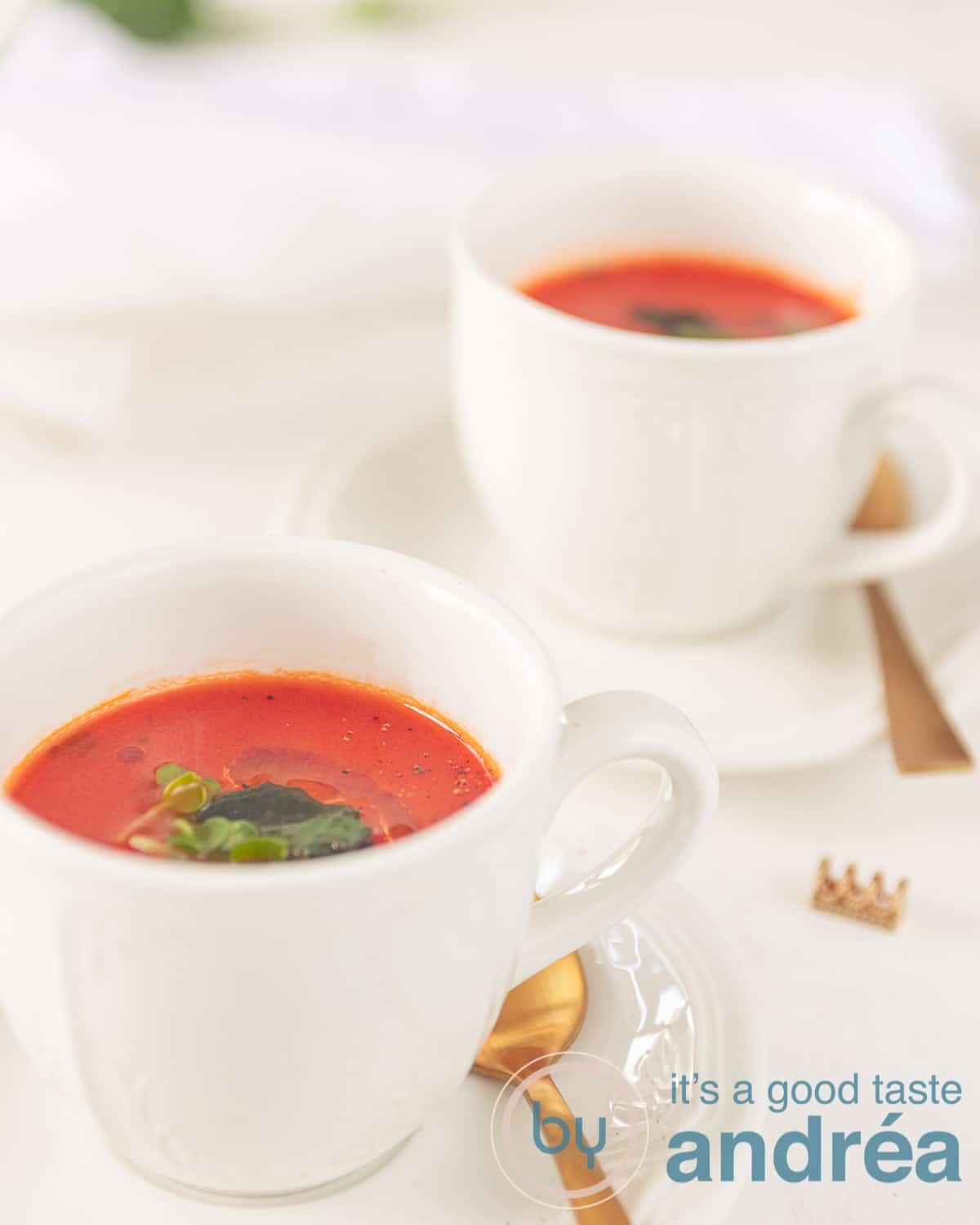 two cups with Rich tomato soup and golden spoons
