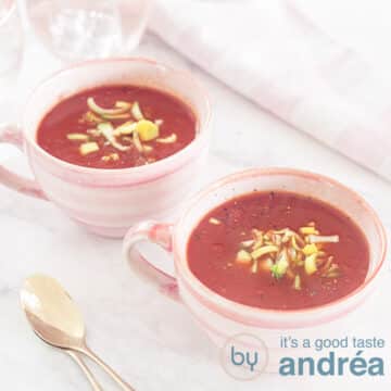 A square photo with two pink cups filled with tomato leek soup. A white background