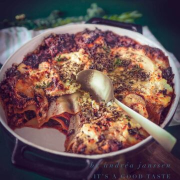 sausage and kale lasagna in a black casserole dish. A bit taken out. A golden spoon. A dark green background
