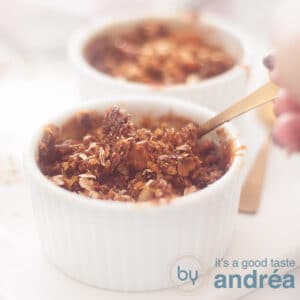 A square photo of two ramekins filled with apple pie granola. A hand takes out a spoon.
