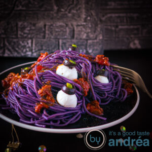 A square photo with a plate loaded with purple spaghetti bolognaise and mozzarella eyeballs.