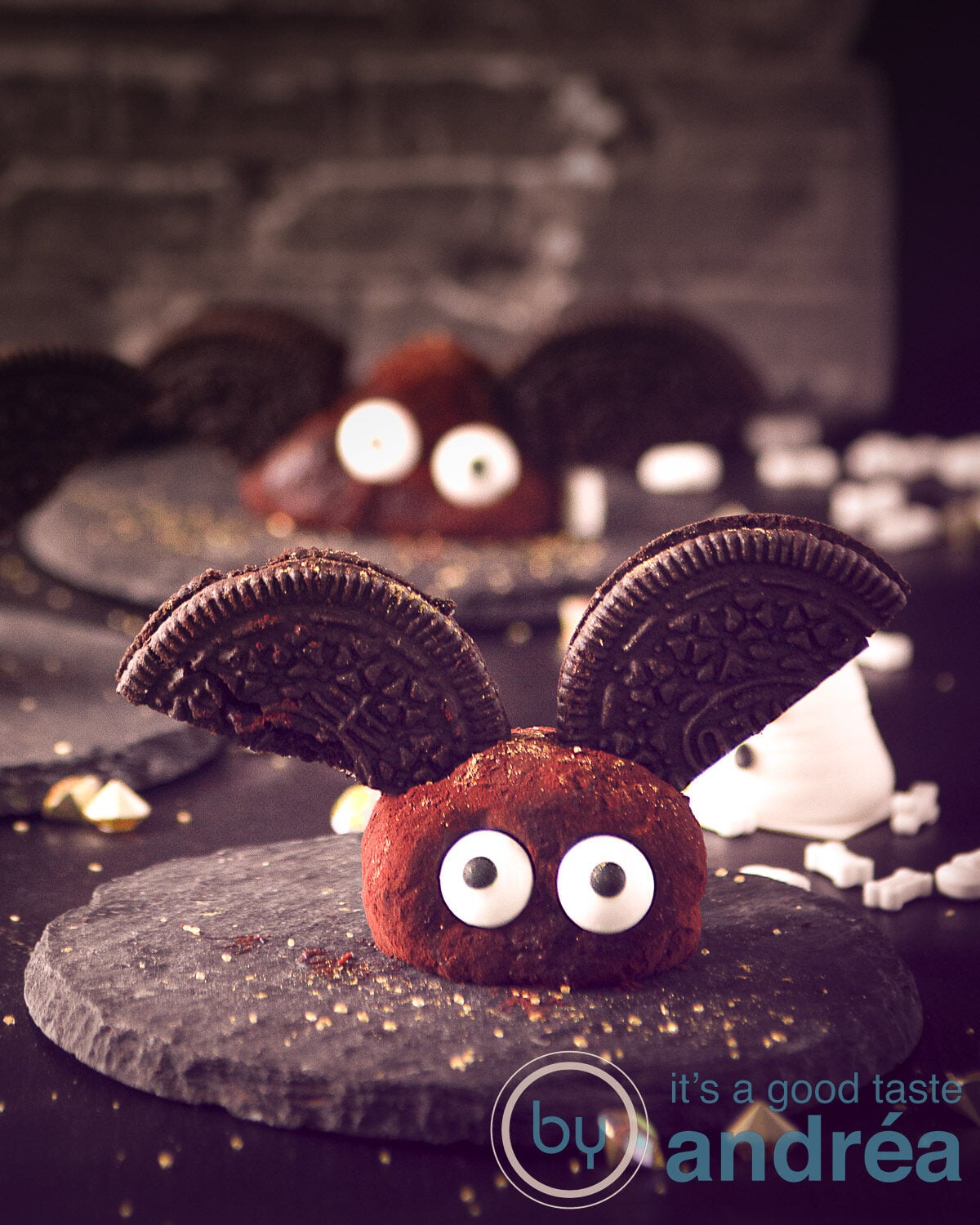 A grey small stone with a truffle with sugar candy eyes and oreo wings dressed like a bat. More in the dark background