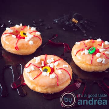 A square photo of three donuts with an eye decoration. On a black background.