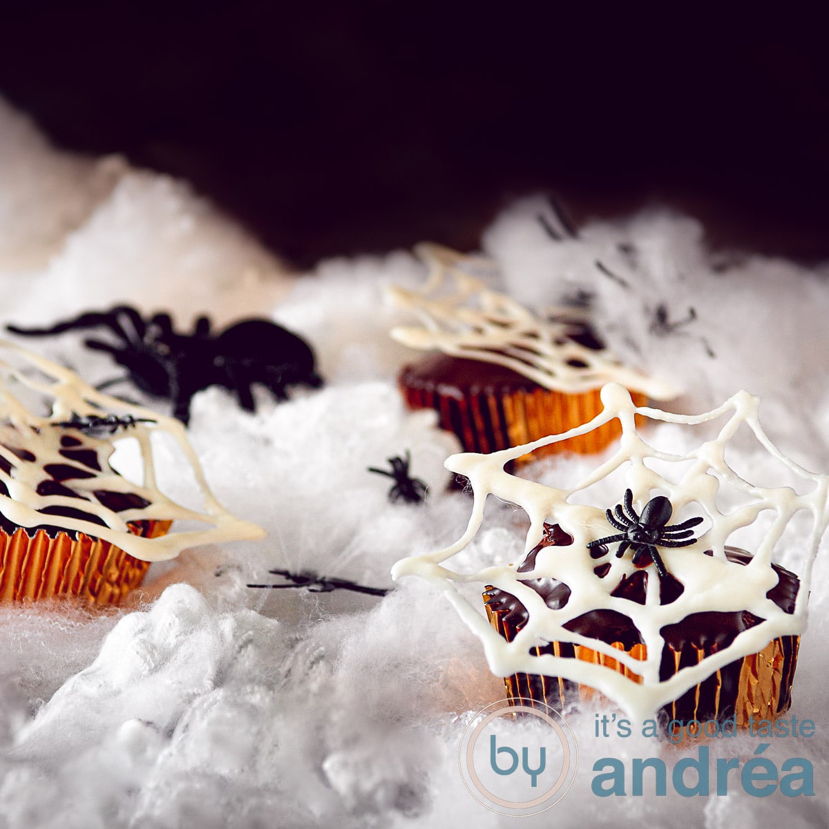 a square photo of nutella cupcakes with white chocolate spiderwebs on a white cloudy ground.