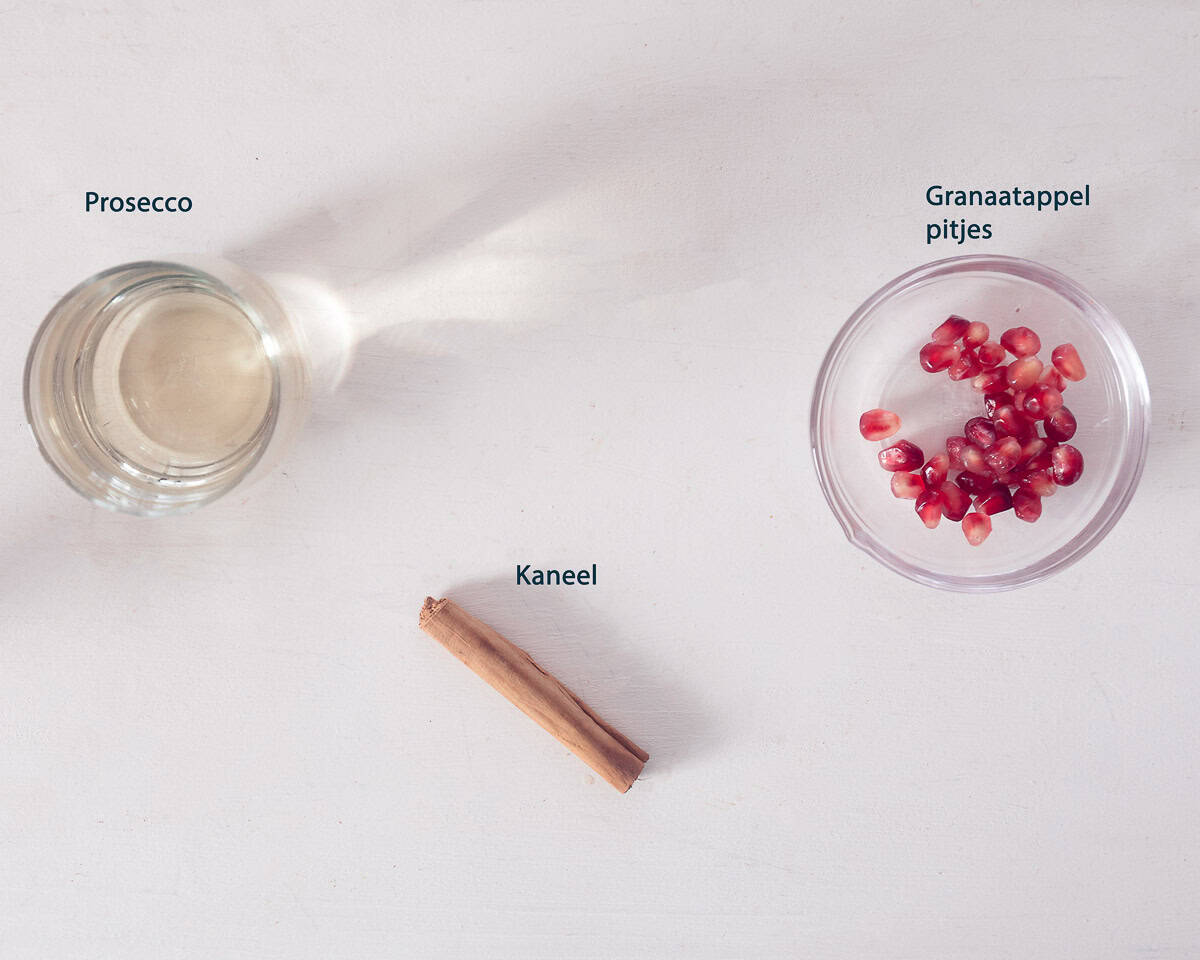 Ingredienten Prosecco cocktail met Granaatappel en Kaneel op een witte ondergrond met tekstbeschrijving.
