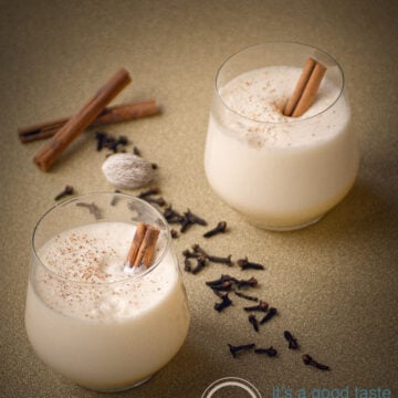 traditional egg nog in two glasses on a golden underground. Some spices are scattered around.