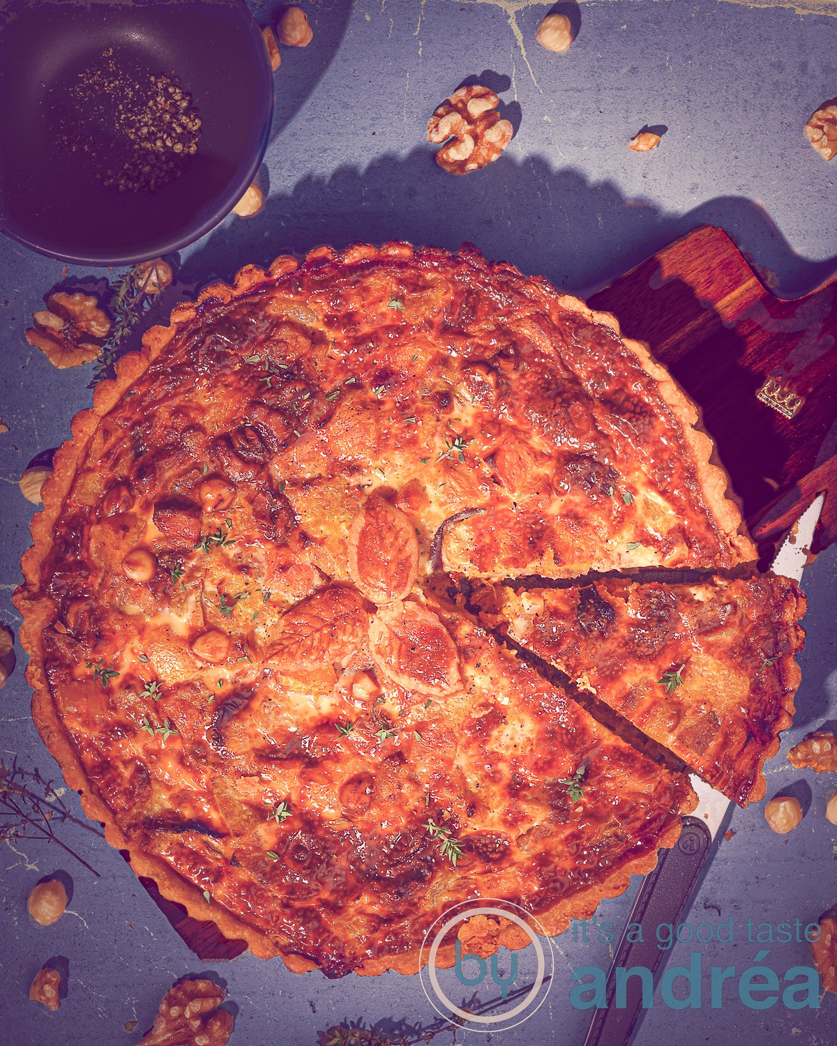 Een quiche met bladerdeeg erbovenop (blad vorm) waar een punt is uitgesneden op een blauwe ondergrond.