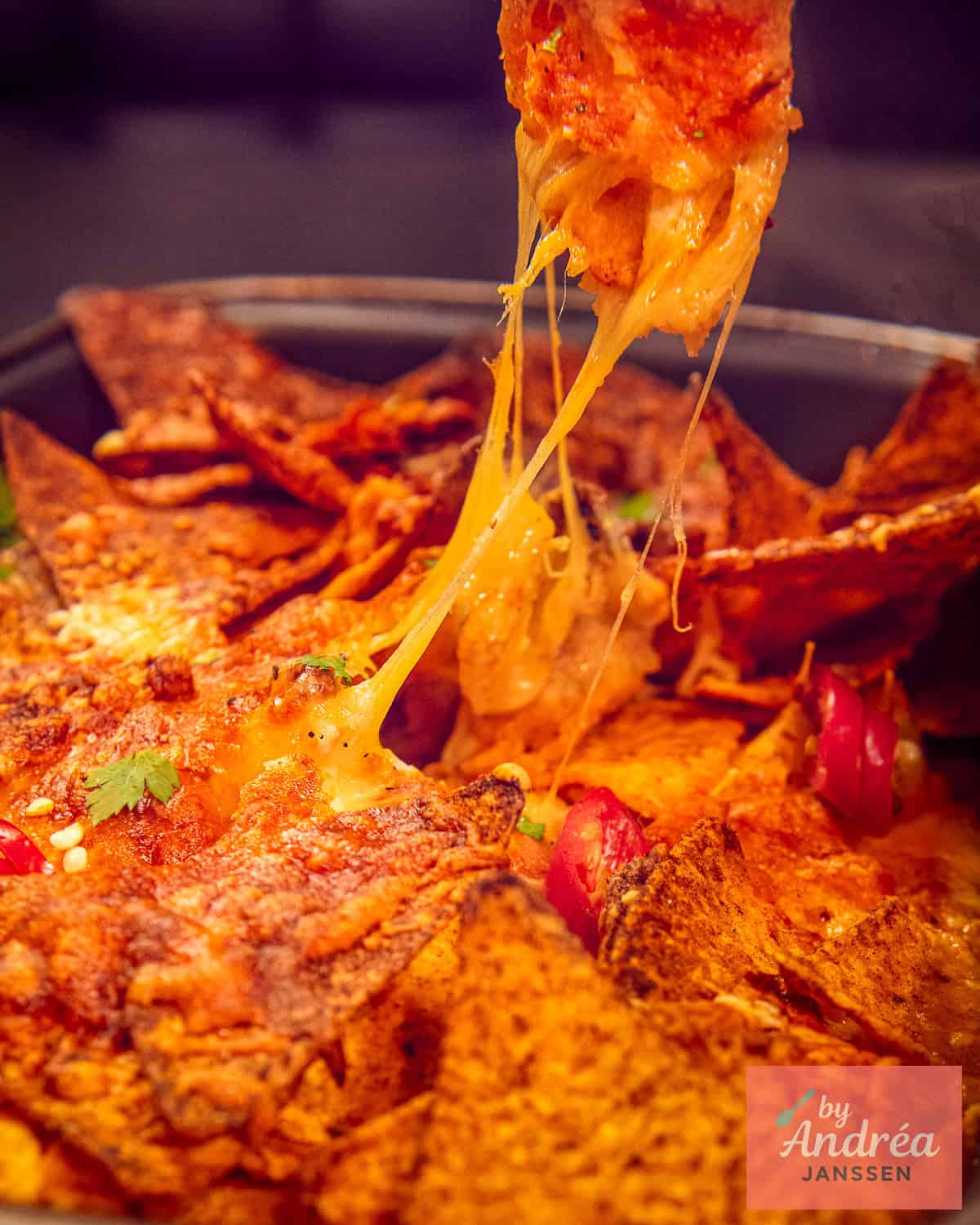 A nacho pulled up full of cheesy threads.