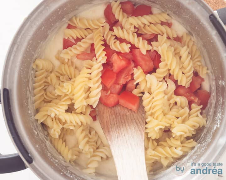 Pasta and tomatoes are mixed with the sauce in a pan.
