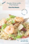 Part of a white plate filled with pesto orzo with parmesan, tomato, string beans and shrimp. A fork taking a bite. A text overlay describing the picture