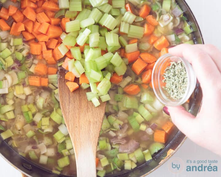 A frying pan with vegetables to which herbs are added.