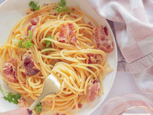 A square picture taken from above from a white plate with no cream pasta carbonara. A fork pricks in the spaghetti