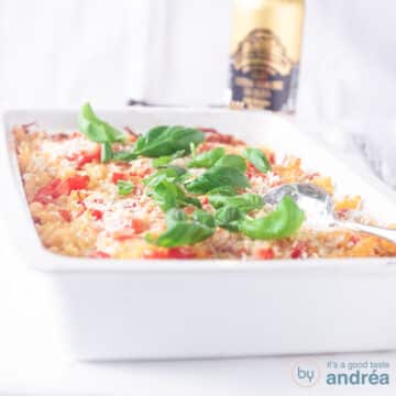A square photo with a white baking dish filled with a pasta casserole with tomatoes, mascarpone and basil. A white background.